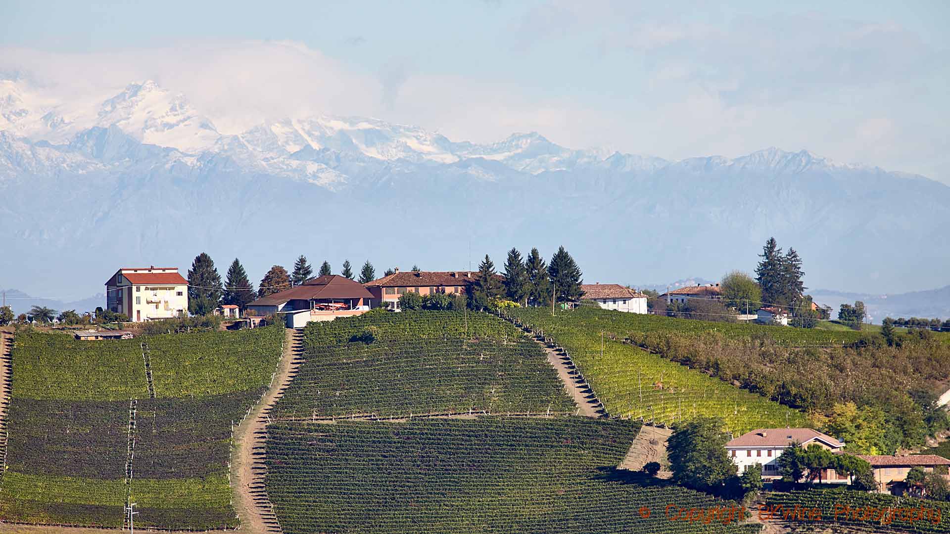 Vineyards, a village on a hilltop and snowy mountains in Piedmont