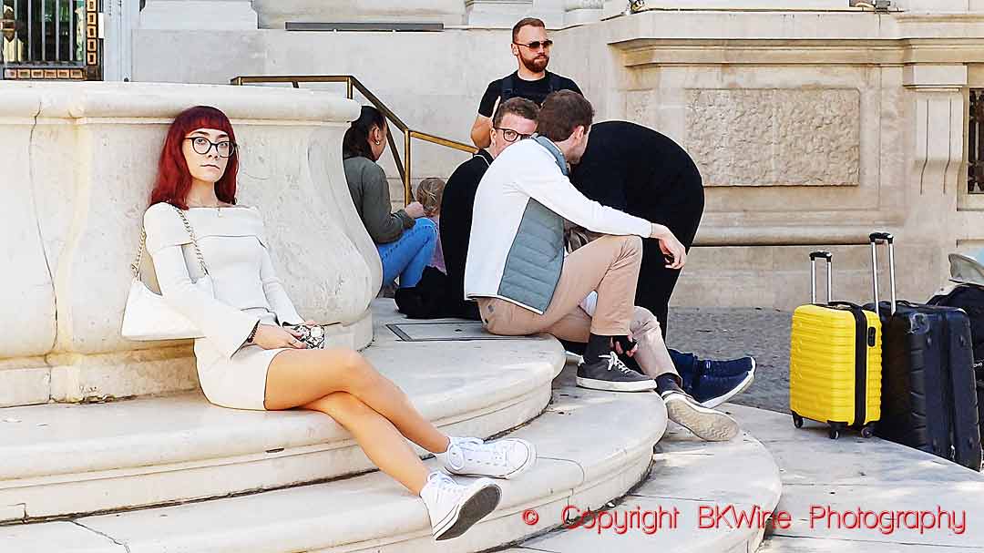 People sitting by a fountain in Sevilla, some with suitcases