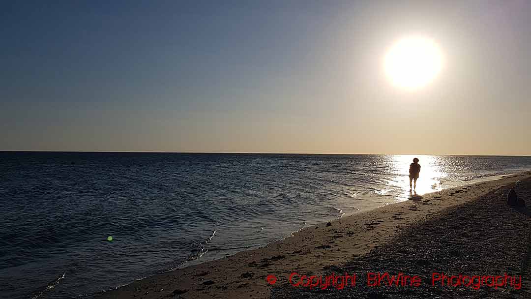 A lone person standing in the sun reflections along the sea on a beach